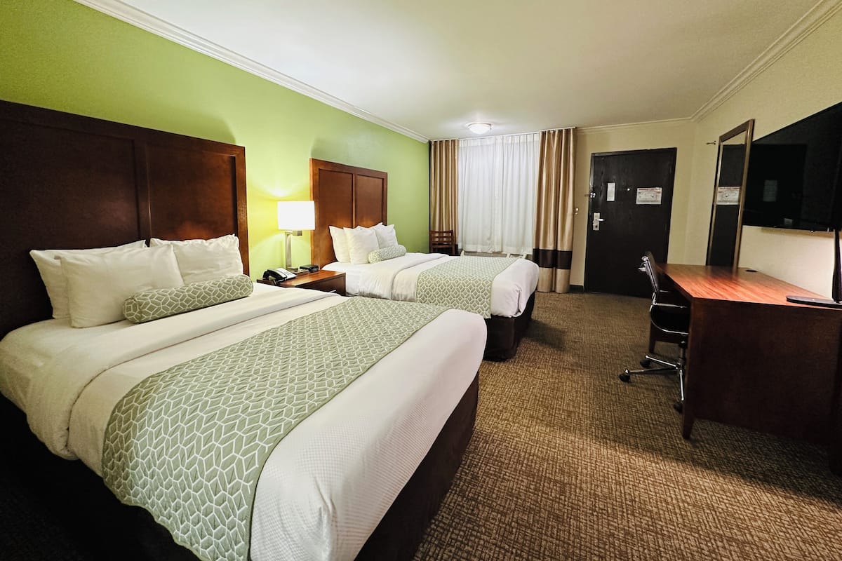 A hotel room with two beds, a desk, a chair, a lamp, and a television.