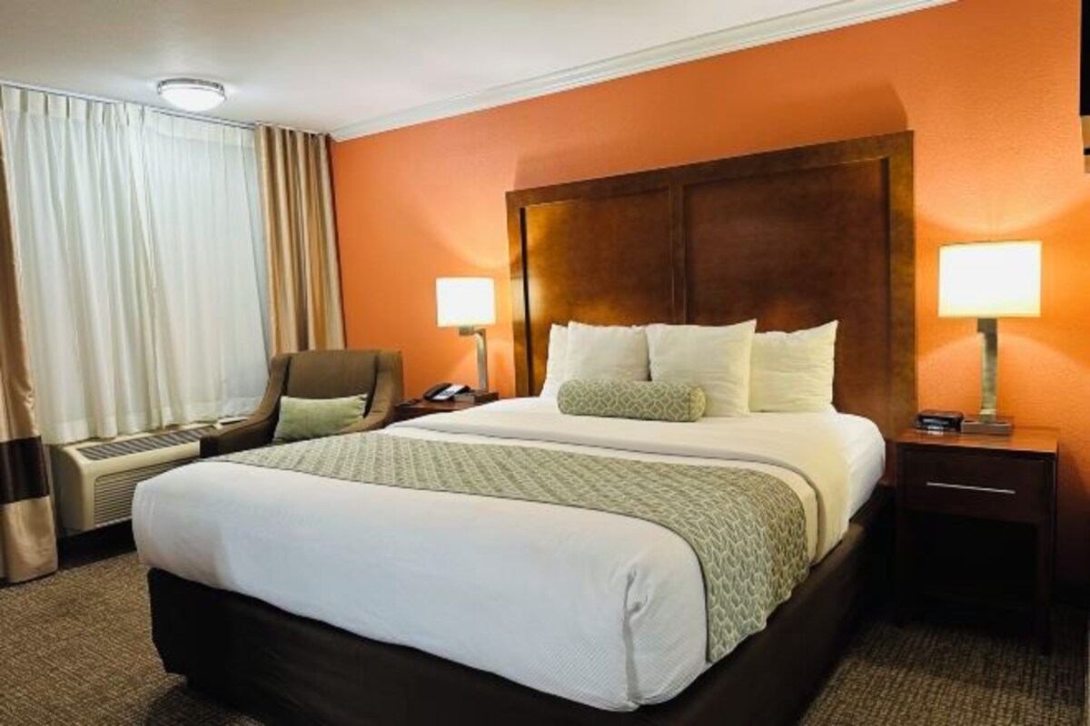 Une chambre d’hôtel avec un grand lit, deux tables de chevet, une chaise, un bureau et une fenêtre avec des rideaux.