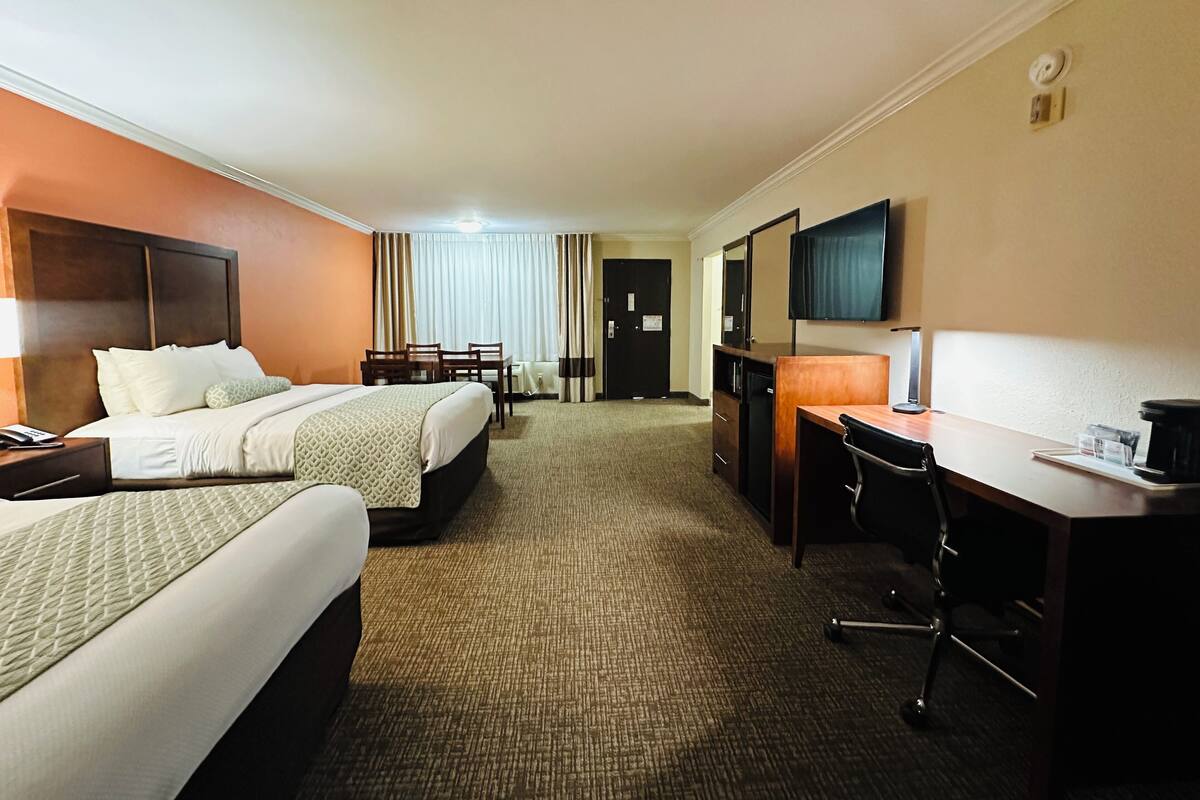 A hotel room with two beds, a desk, a chair, a television, and a minibar.