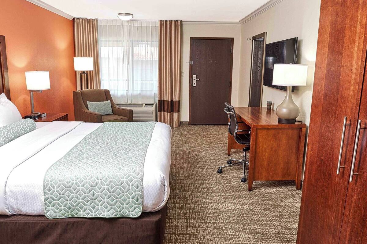 A hotel room with a large bed, a desk, a chair, a TV, and a wardrobe.