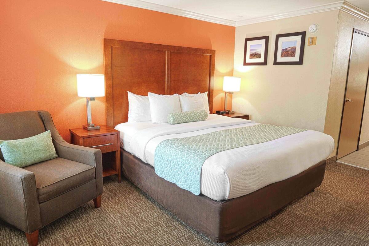 A hotel room with a large bed, two bedside lamps, a chair, and a door.