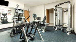 Un gimnasio con máquinas de cardio, equipo de entrenamiento con pesas y un espejo.