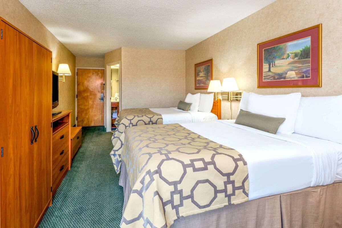 A hotel room with two beds, a wardrobe, a television, and a painting on the wall.
