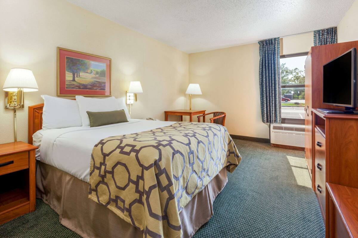 A hotel room with a bed, two bedside tables, lamps, a television, and a window with curtains.