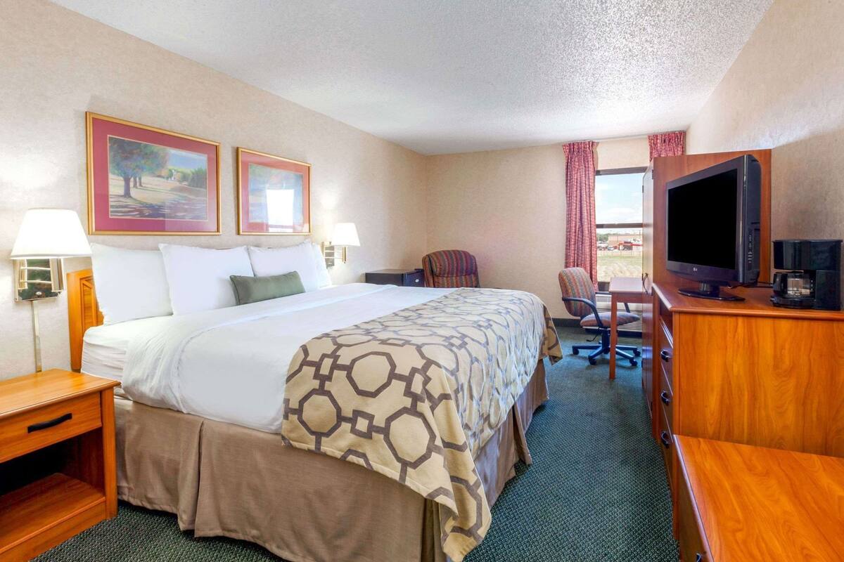 A hotel room with a bed, two paintings, a desk with a TV, and a chair.