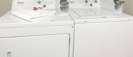 A front view of a Whirlpool washer and dryer set in a laundry room with patterned curtains in the background.