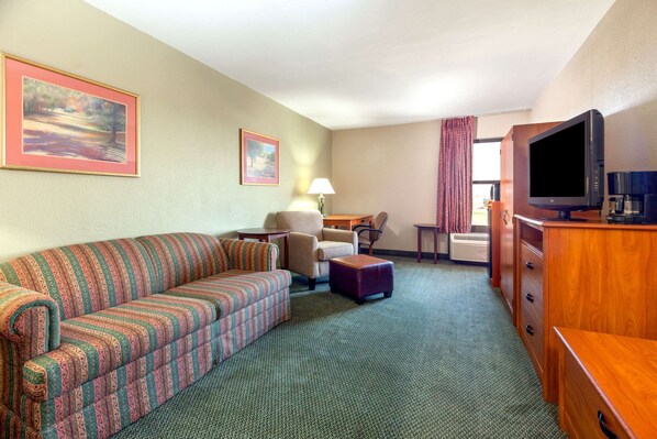 A hotel room with a striped sofa, a chair, a small table, a television, and a wooden cabinet. - Baymont by Wyndham Amarillo East (Amarillo)