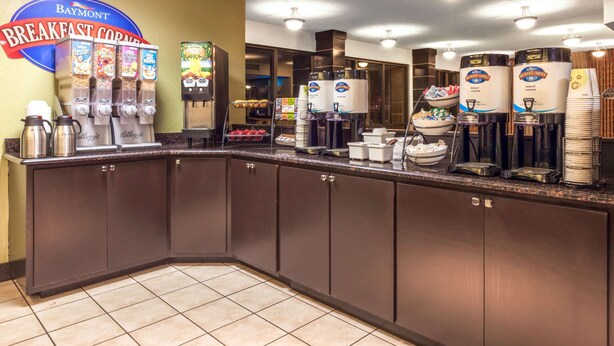 Una barra de desayuno con varios dispensadores de café, un dispensador de cereales y un cartel que indica Baymont Breakfast Corner.