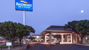Un Baymont Inn & Suites con un cartel iluminado grande, una zona de estacionamiento techada y un edificio de techo rojo.