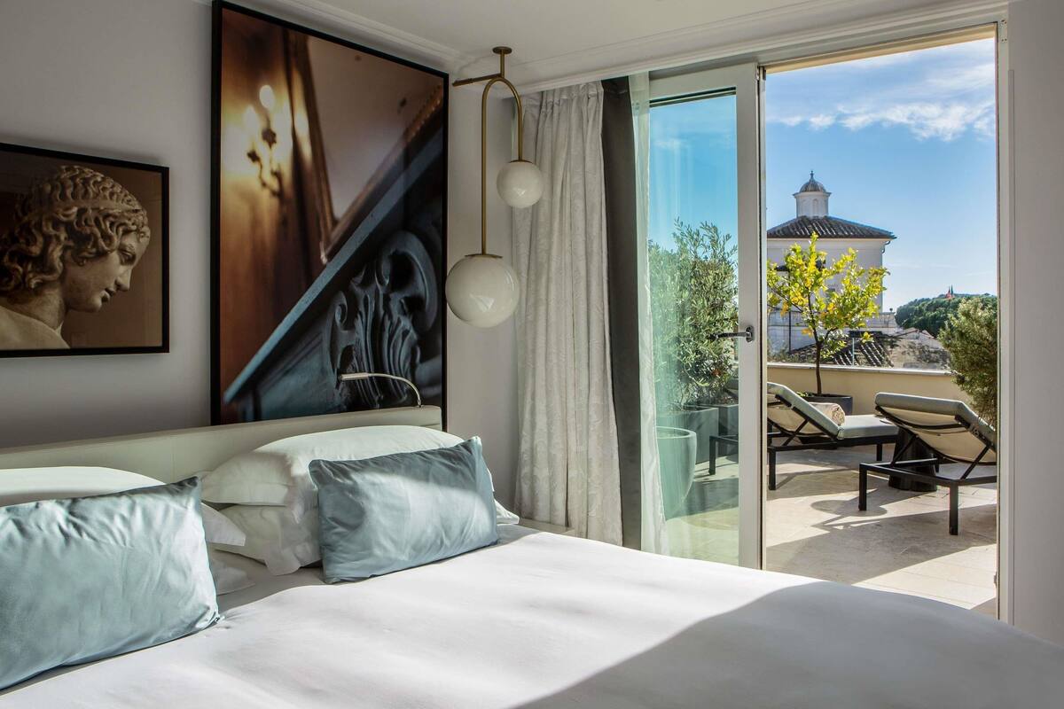 Quarto com cama grande, um quadro e vista para uma varanda com cadeiras.