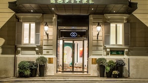 The entrance of the Sofitel hotel with a prominent sign, a grand facade, and a series of potted plants at the entrance. - Sofitel Rome Villa Borghese (Rome)