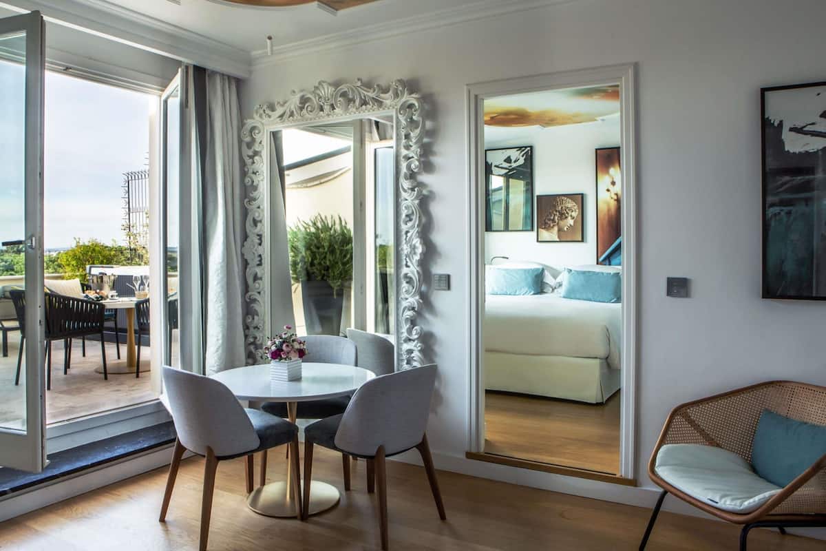 A modern hotel room with a dining area, a large mirror, and a view of the outdoors.