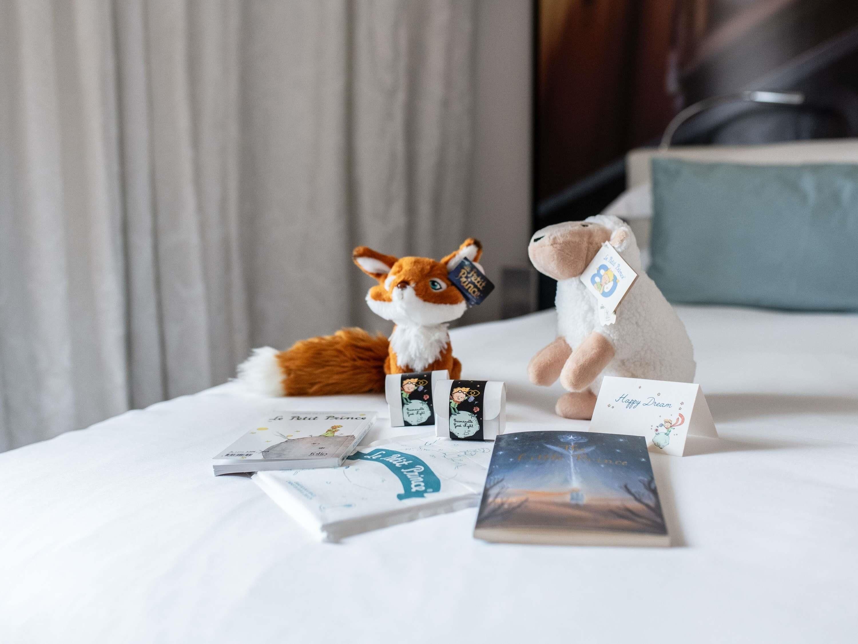 Una cama con una colcha blanca, un peluche, varios libros y un animal de peluche.