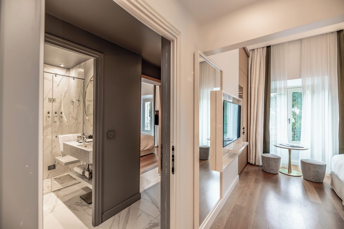A modern hotel room with a marble bathroom, a bed, a TV, and a balcony with curtains.