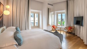 A hotel room with a large bed, a TV, a balcony view, and a dining area with chairs. - Sofitel Rome Villa Borghese (Rome)