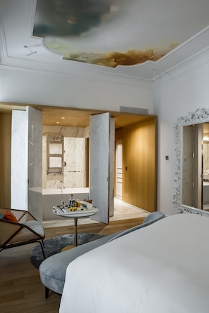 A modern hotel room with a large bed, a small round table with toiletries, a mirror with an ornate frame, and a view of the bathroom through an open door. - Sofitel Rome Villa Borghese (Rome)
