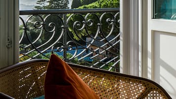 Un balcón con barandilla de hierro forjado, una silla de mimbre con cojín y vistas a una cúpula y follaje.