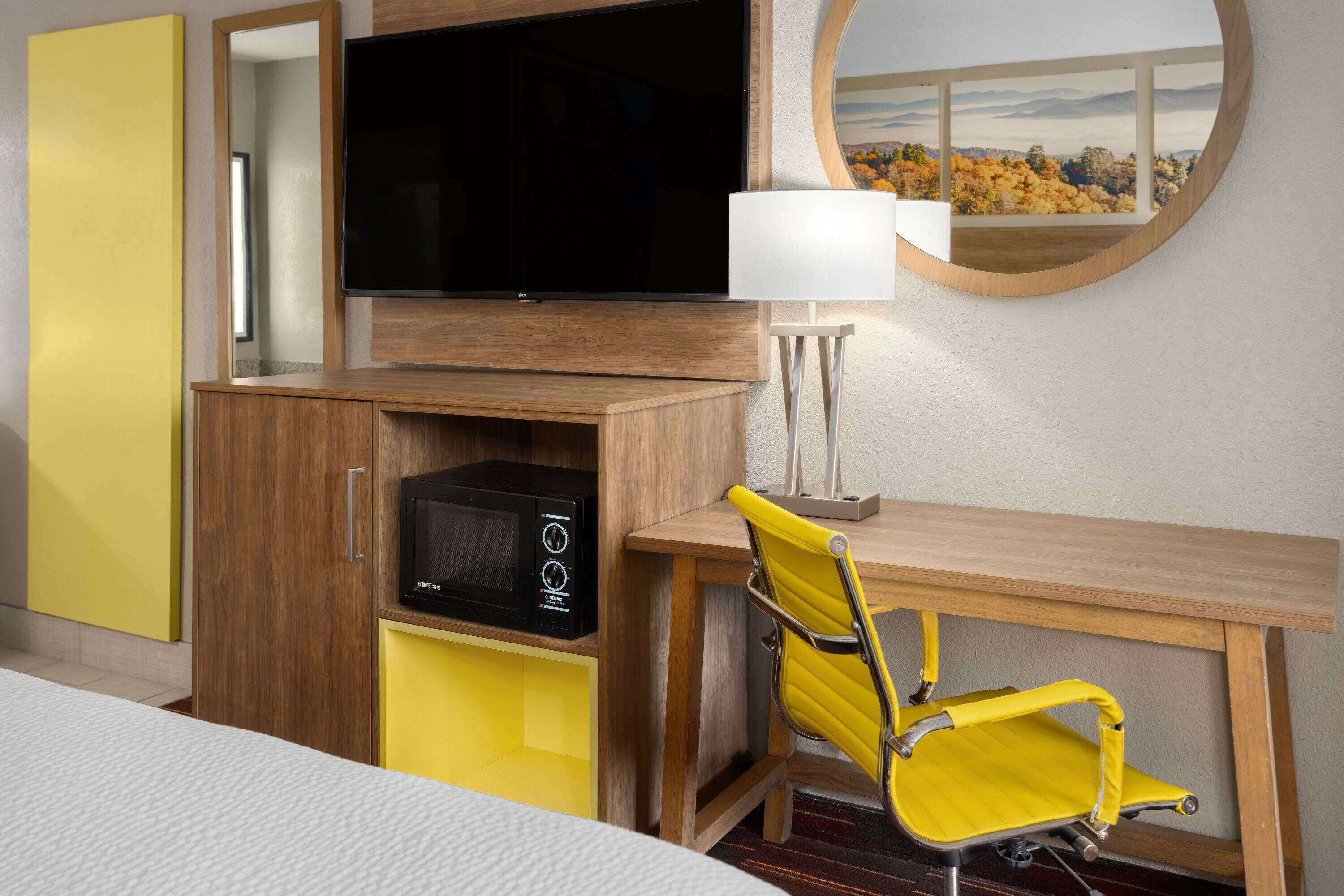 A hotel room with a TV, a desk, a chair, a lamp, and a view of a mountainous landscape.