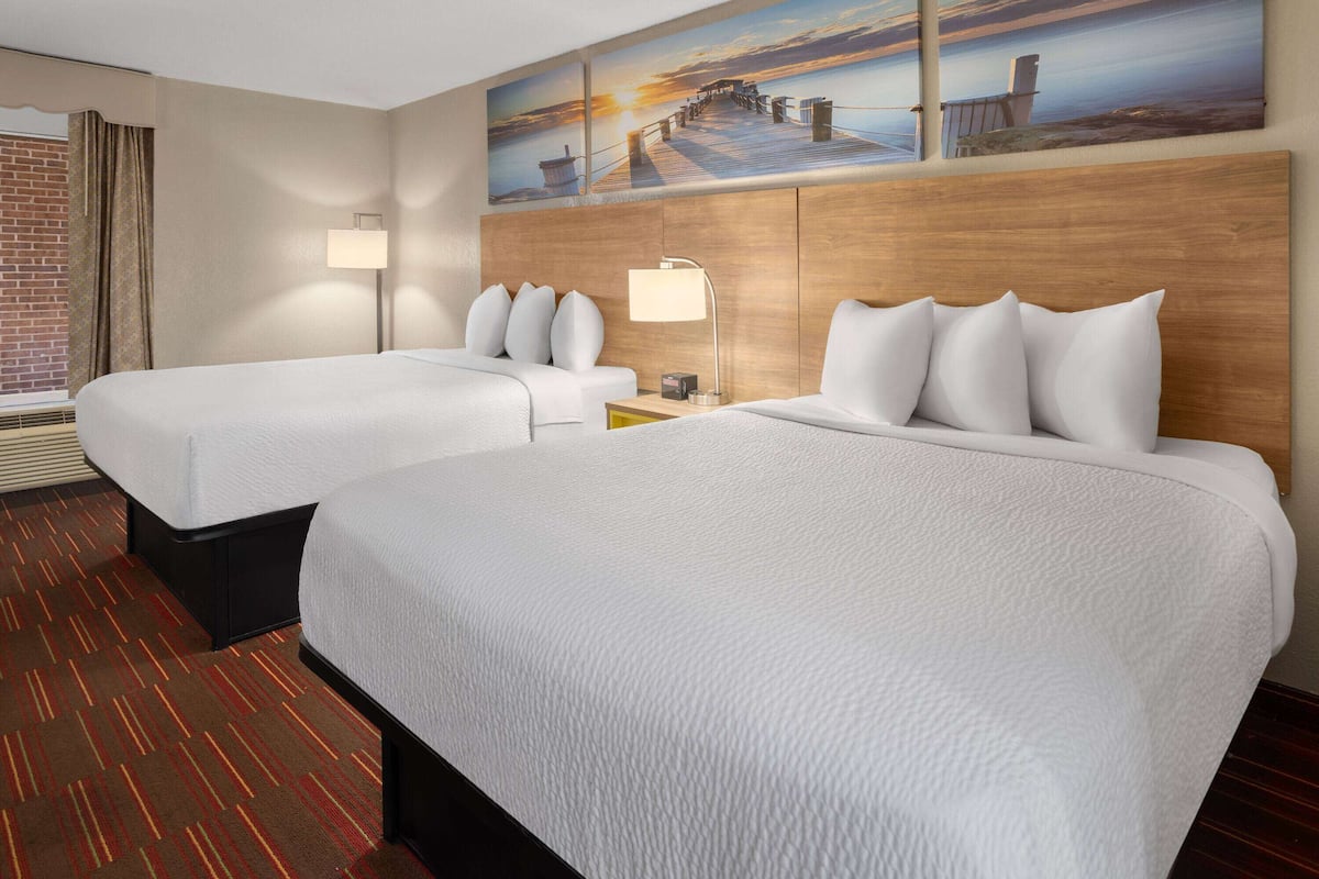 A hotel room with two beds, a wooden headboard, a brick wall, and a large window with curtains.