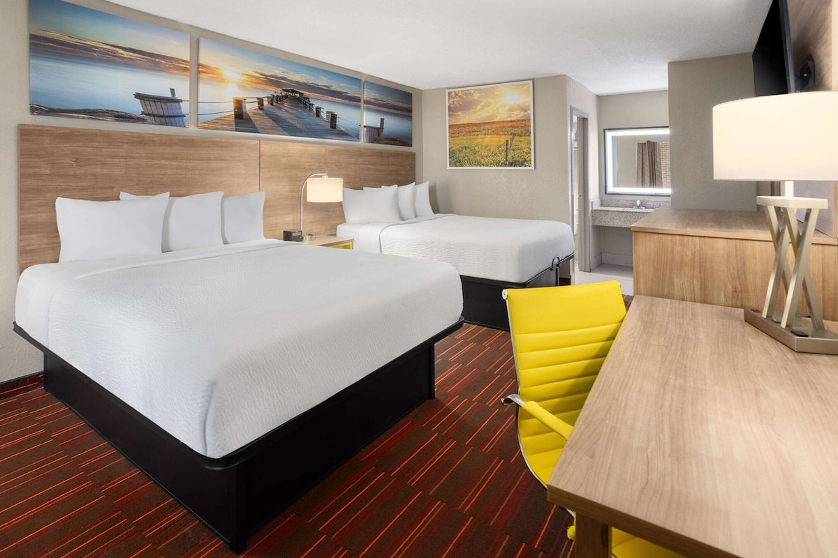 A hotel room with two beds, a desk, a chair, a mirror, and artwork on the walls.