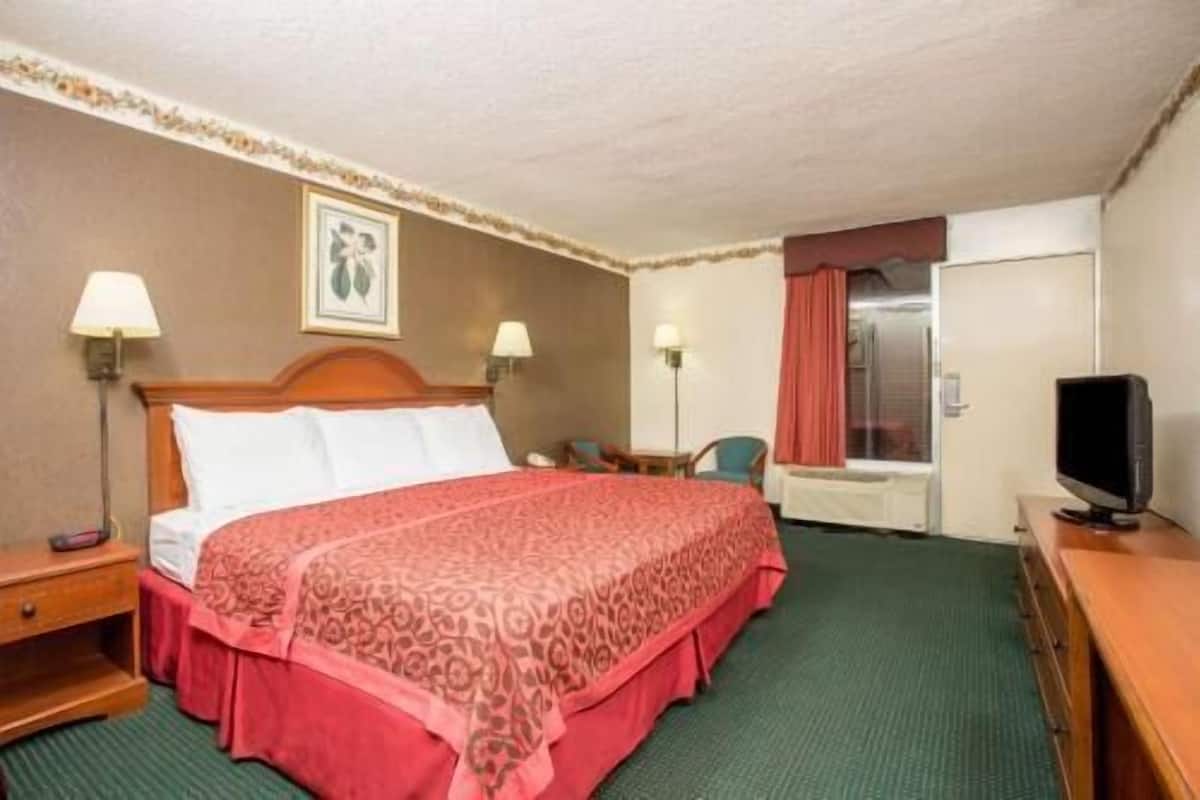A hotel room with a bed, two bedside tables, a desk with a chair, a television, and a window with curtains.