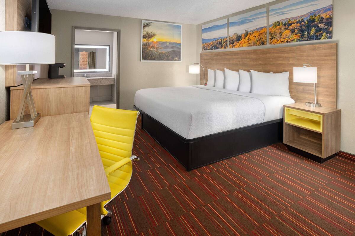 A hotel room with a bed, a desk, a chair, and a nightstand.