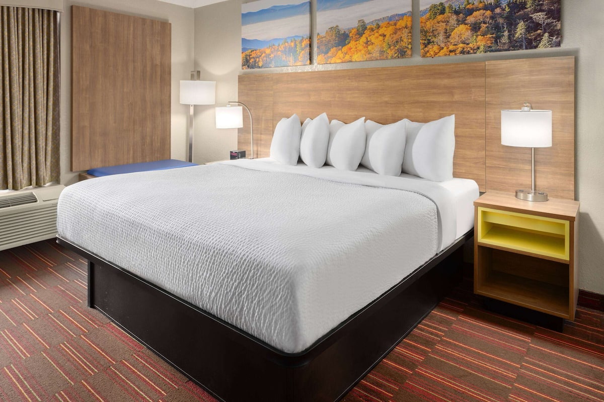 A hotel room with a large bed, two bedside tables with lamps, a wooden headboard, and a view of autumn foliage.