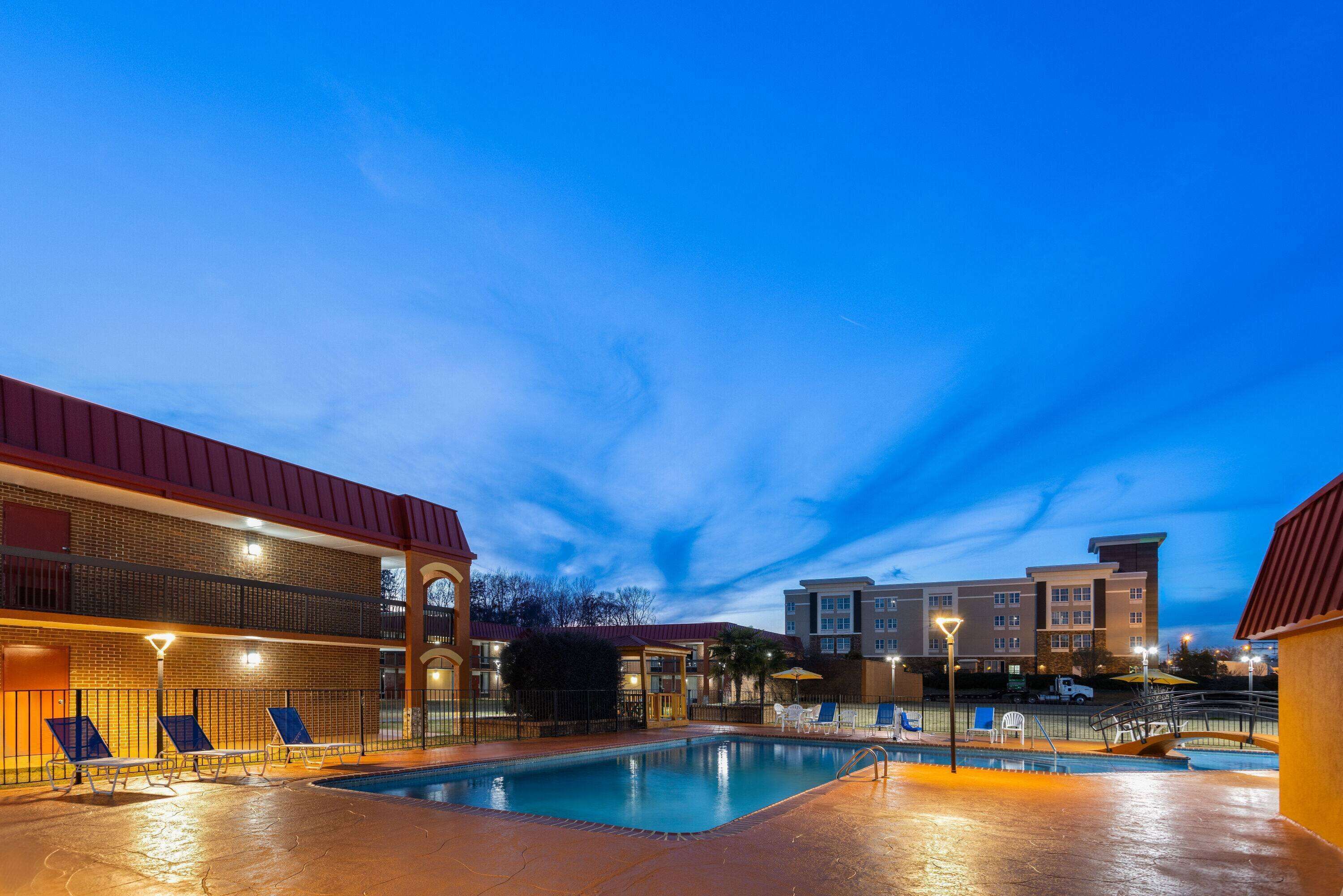 Zona de piscina con sillones de descanso y un edificio de dos pisos al fondo.