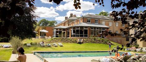 A poolside area with lounge chairs, a swimming pool, and a building with large windows.