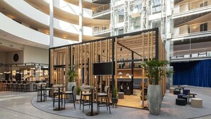 A modern indoor space with a central seating area, a large screen, and a staircase leading to upper levels. - NH Düsseldorf City (Düsseldorf)