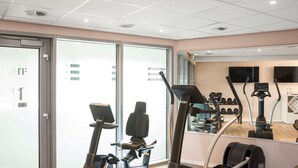 A modern gym with cardio equipment, large windows, and a mirrored wall. - NH Düsseldorf City (Düsseldorf)