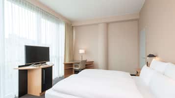 Una habitación de hotel con una cama, un escritorio, un televisor y una ventana con cortinas.