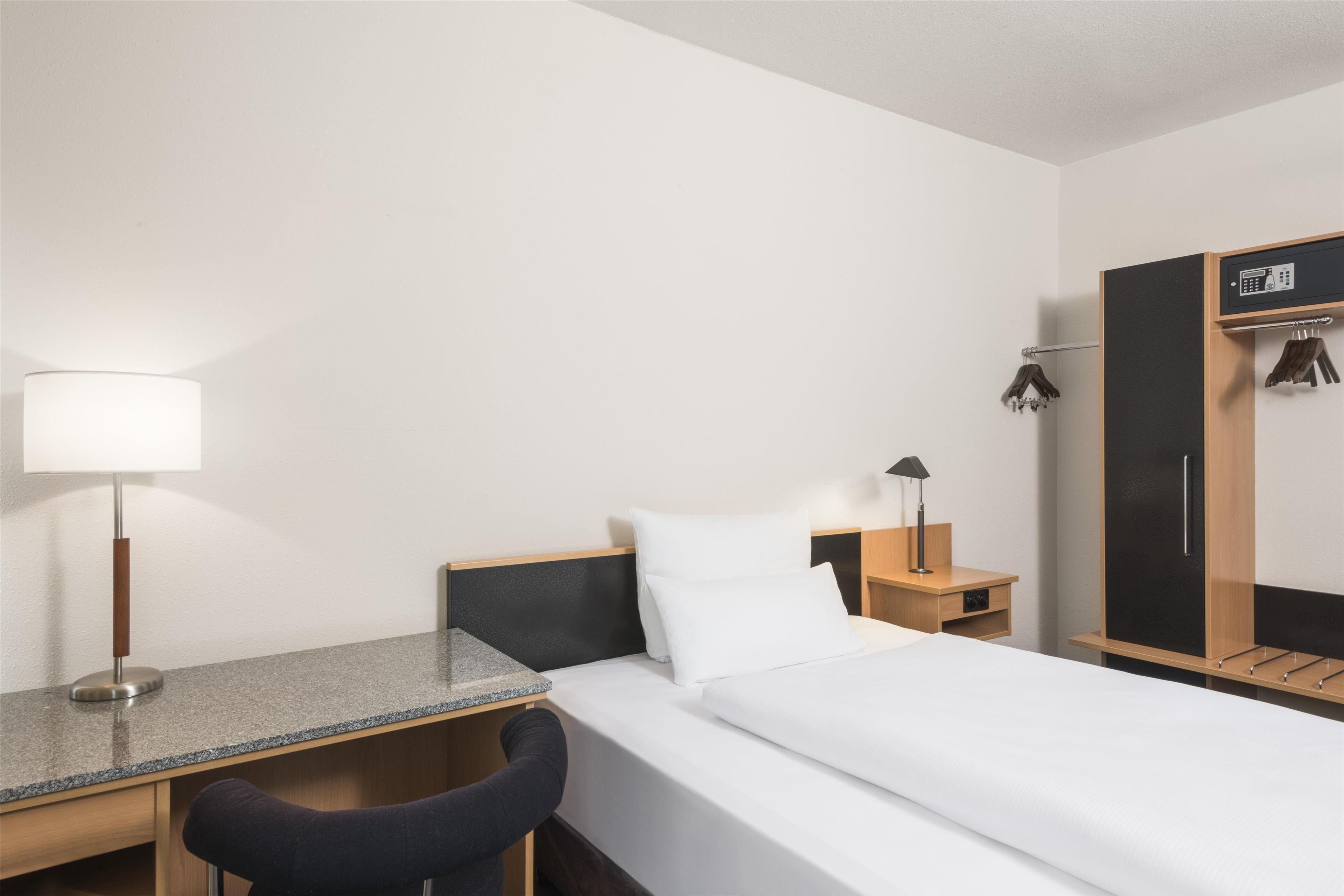 Ein Hotelzimmer mit Bett, Schreibtisch, Stuhl, Kleiderschrank und Nachttisch.
