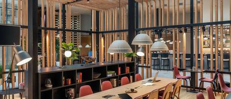 Un interior moderno con techo de madera, estanterías de marco negro y sillas rojas alrededor de una mesa central.