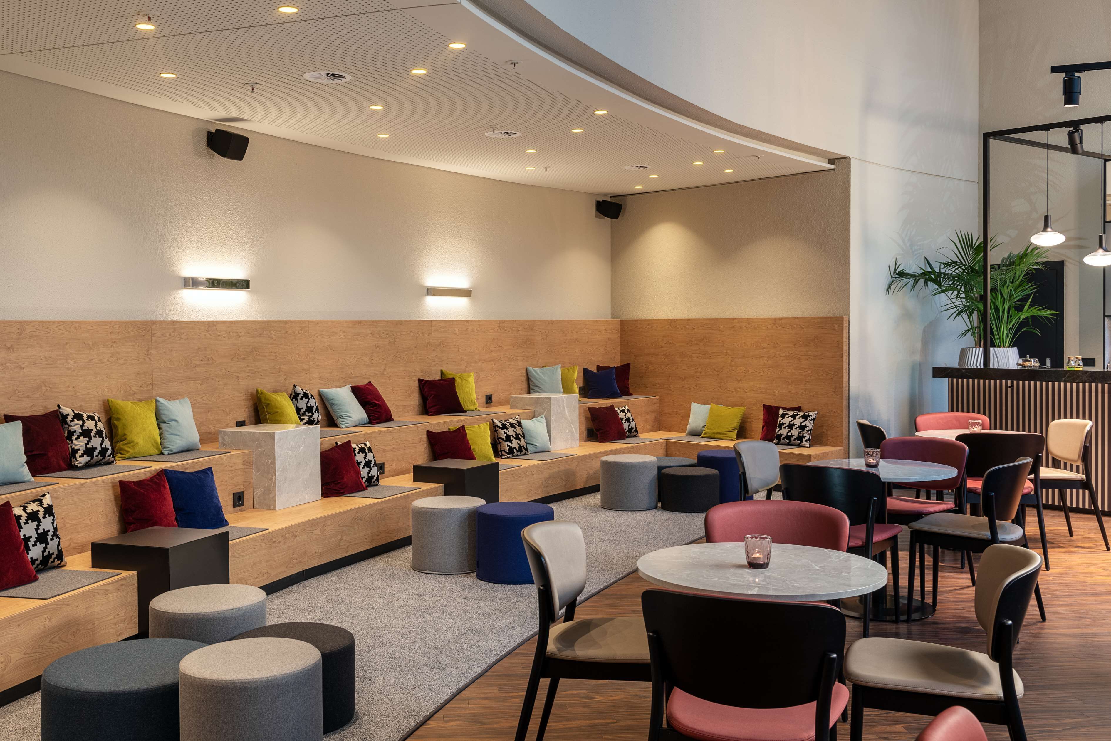 Ein moderner Lounge-Bereich mit Sitzgelegenheiten und Tischen, der verschiedene Farben und eine Wand aus Holz aufweist.