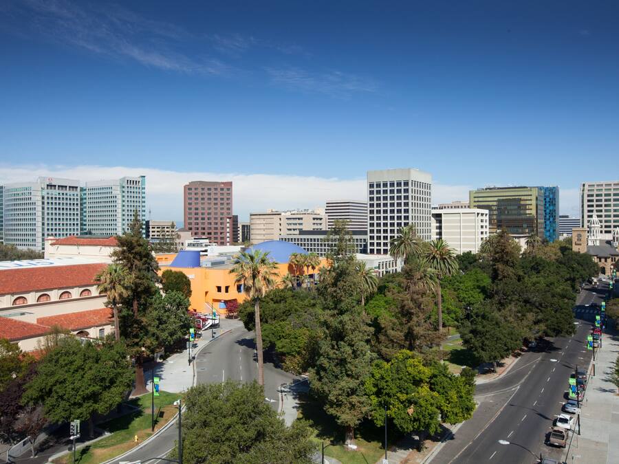 A cityscape with modern buildings, a clear sky, and a street lined with trees.