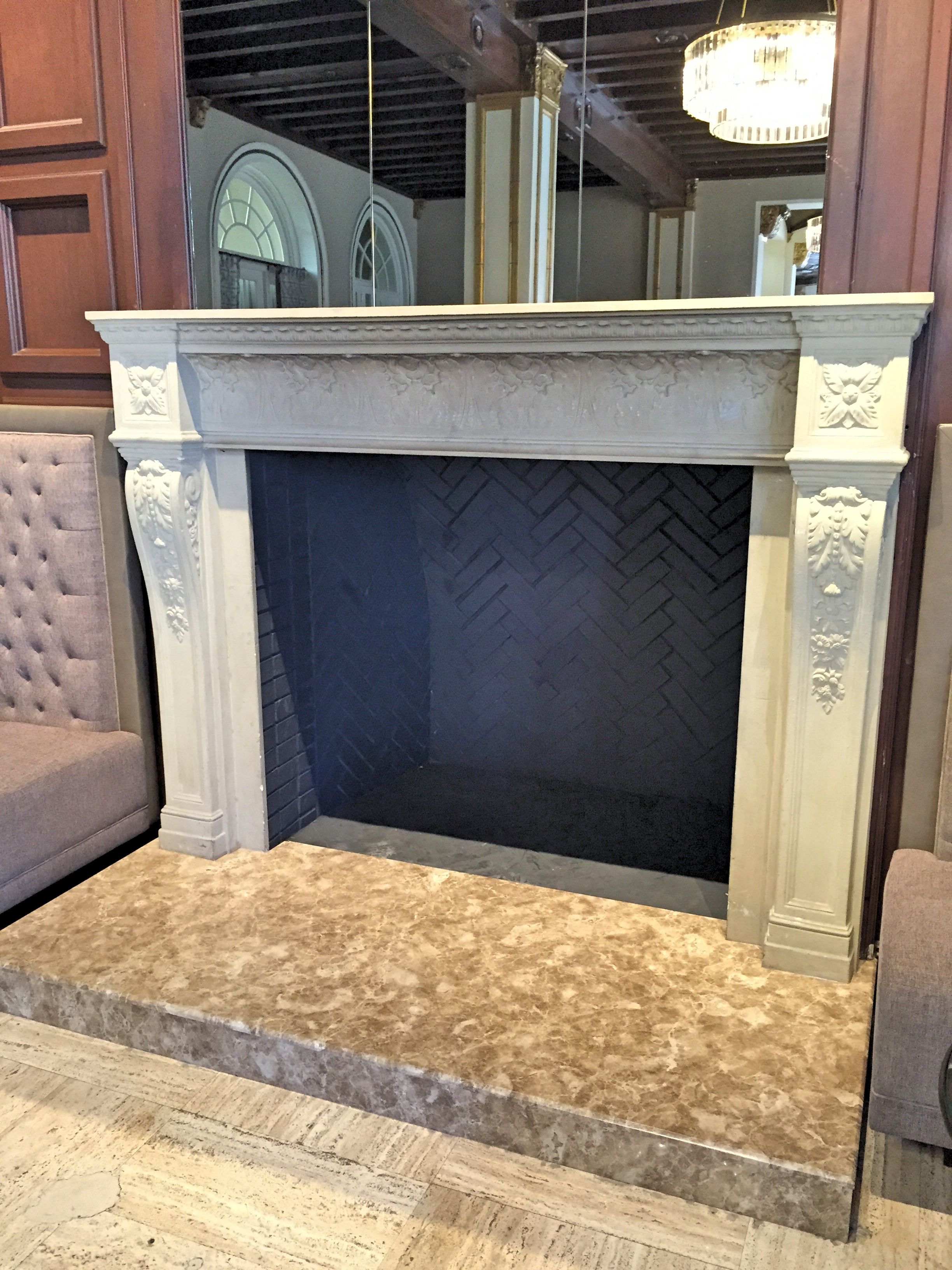 A fireplace with a herringbone-patterned back wall, flanked by ornate white mantelpieces.