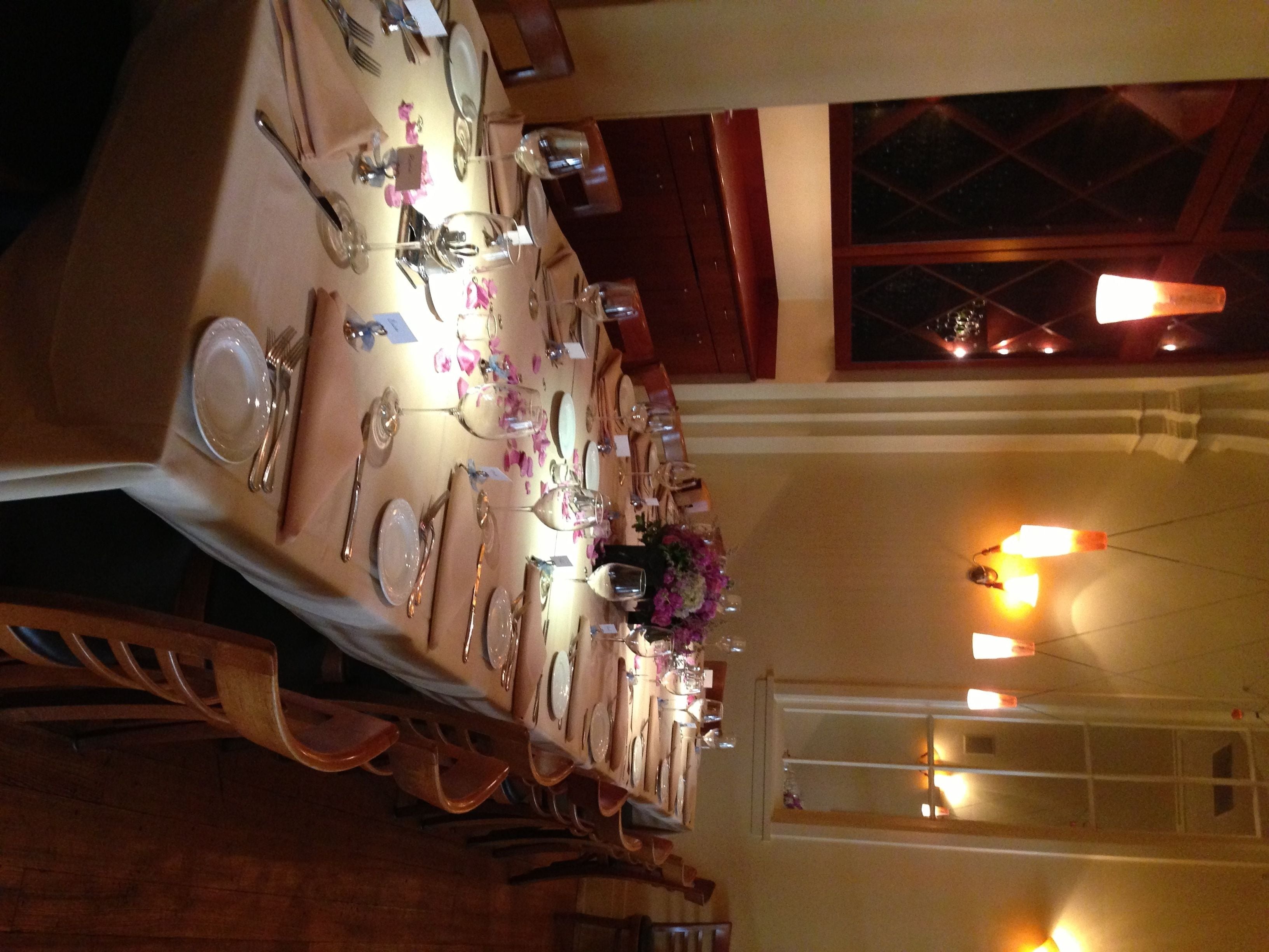 A long dining table set with multiple plates, cutlery, and glasses, with a floral centerpiece.