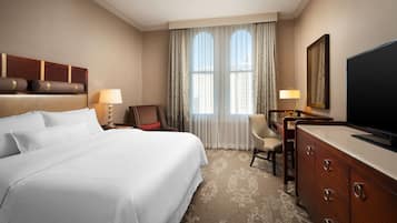 Quarto de hotel com uma cama grande, uma mesa com cadeira, televisão e janela com cortinas.