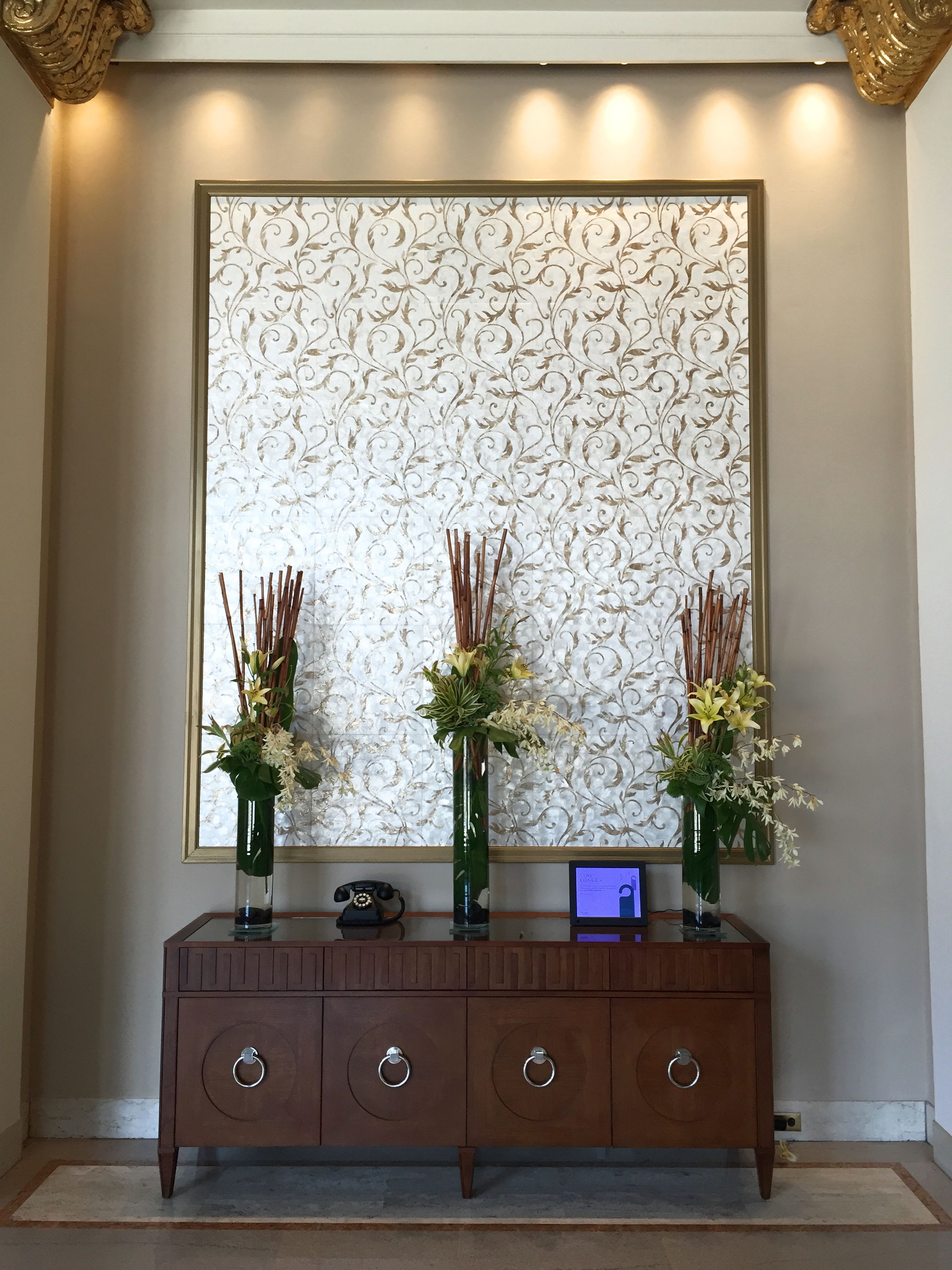 A wooden console table with three vases of flowers, a rotary phone, and a laptop.