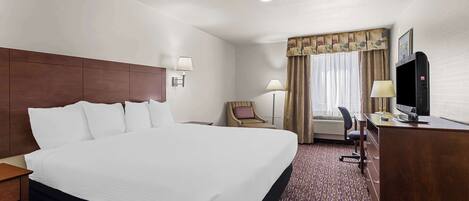A hotel room with a large bed, a desk with a computer, a chair, a lamp, and a television.
