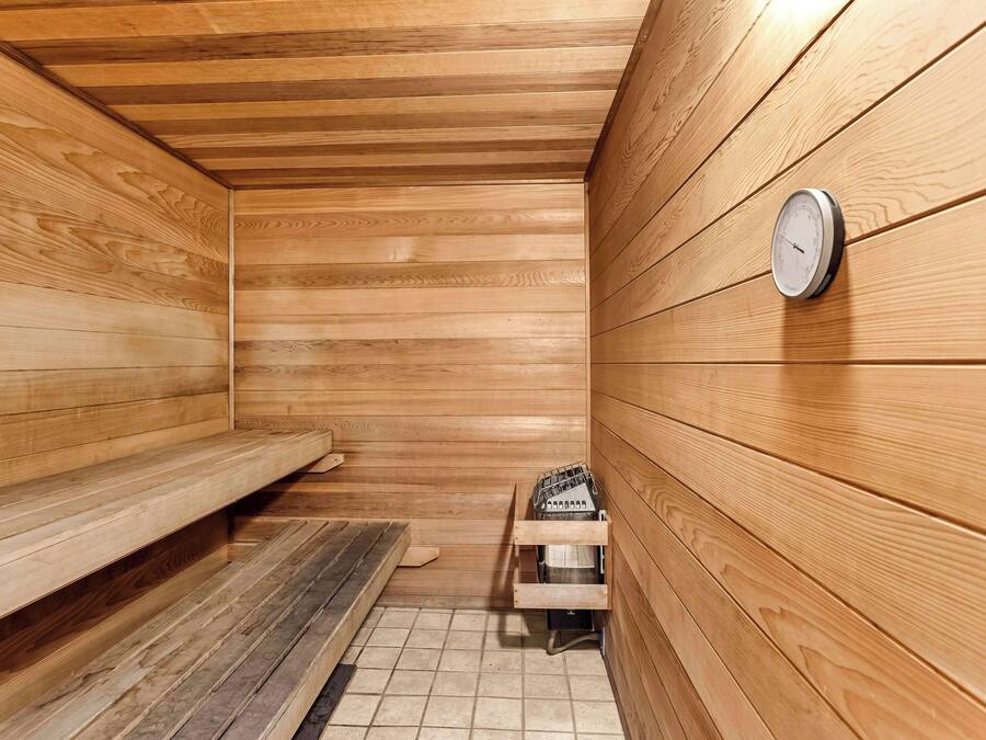Un sauna avec des murs en bois, un banc, un appareil de chauffage et un thermomètre fixé au mur.