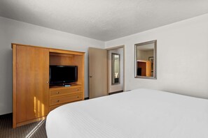 Habitación de hotel con una cama grande, armario de madera, televisor y espejo.