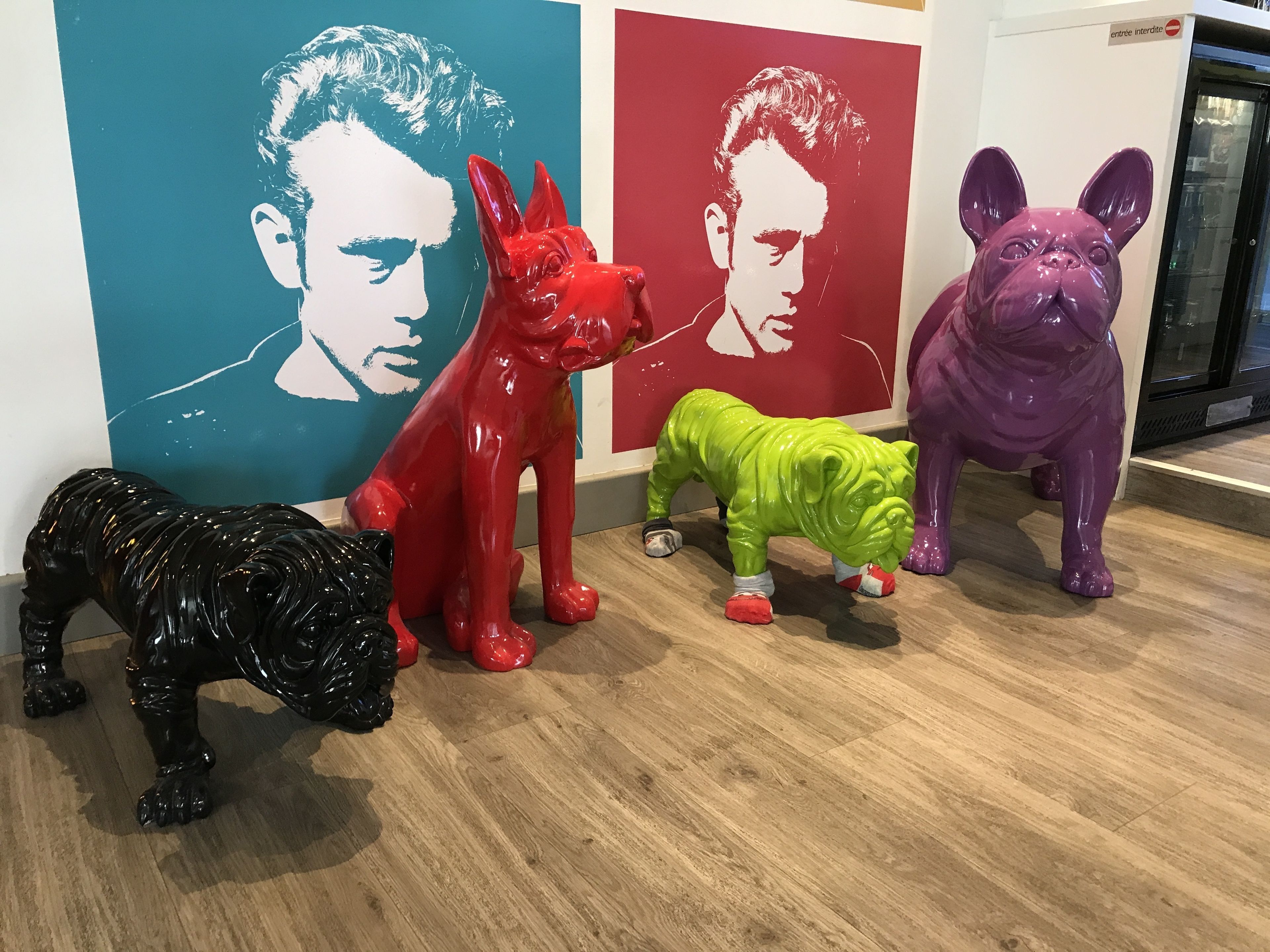 A room with a wooden floor, a black dog statue, and colorful animal statues against a wall with a red and blue mural.