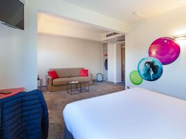 Habitación de hotel con cama, sofá, una mesita, perchero y una pared decorada.