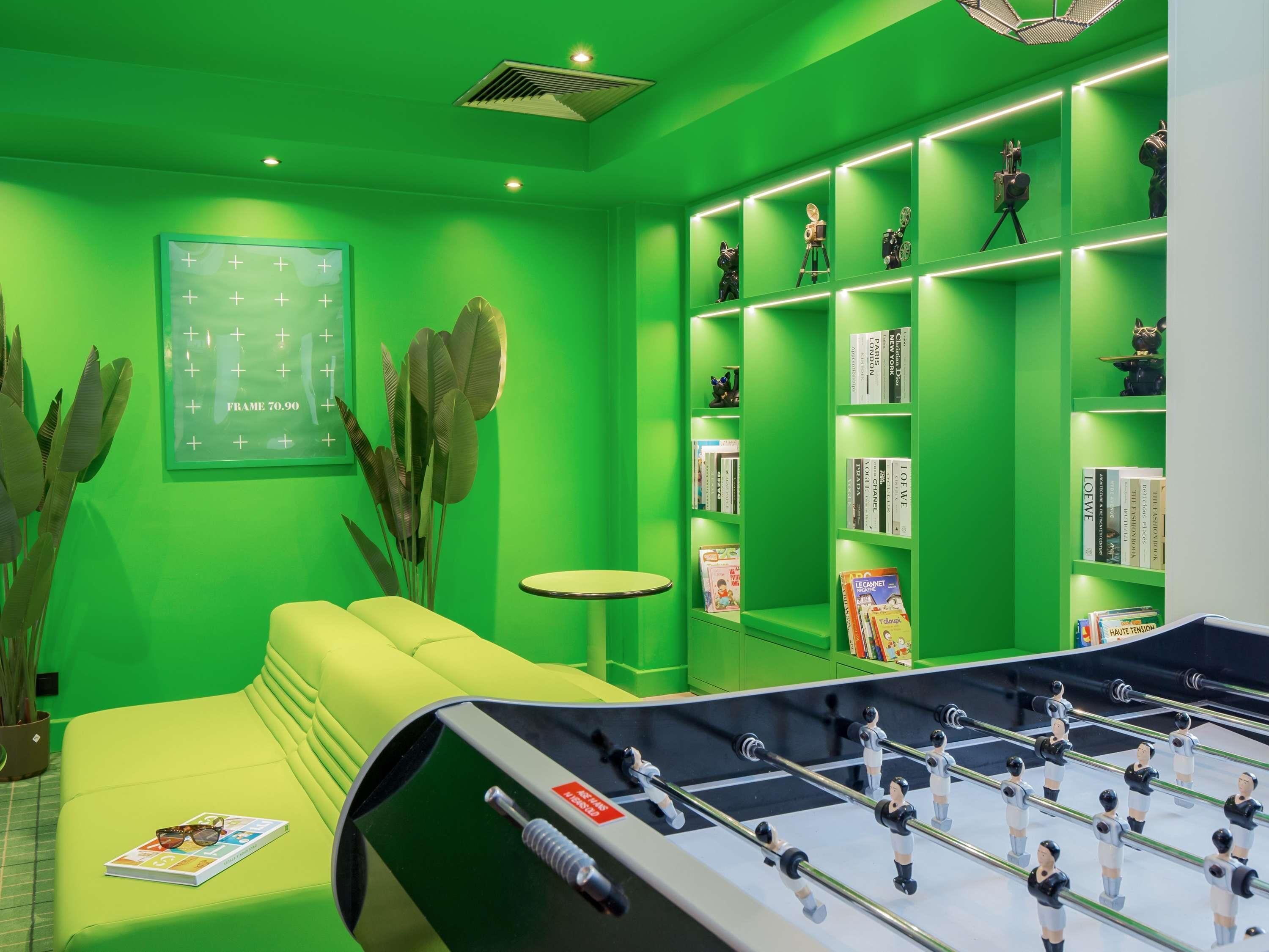 Una habitación con decoración en tonos verdes, una mesa de fútbol de mesa, un sofá, una pequeña mesa redonda y estanterías con libros y objetos decorativos.