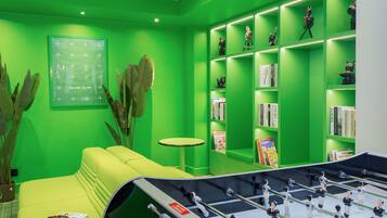 Una habitación con decoración en tonos verdes, una mesa de fútbol de mesa, un sofá, una pequeña mesa redonda y estanterías con libros y objetos decorativos.