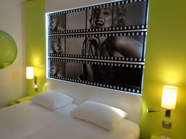 Una habitación de hotel con una cama, dos lámparas de noche, una pared verde y una obra de arte grande en estilo de fotograma de cine.