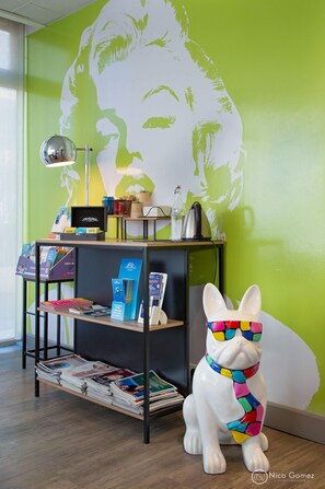 A room with a green wall, a bookshelf with books and magazines, a decorative dog statue, and a lamp. - ibis Styles Cannes le Cannet (Le Cannet)