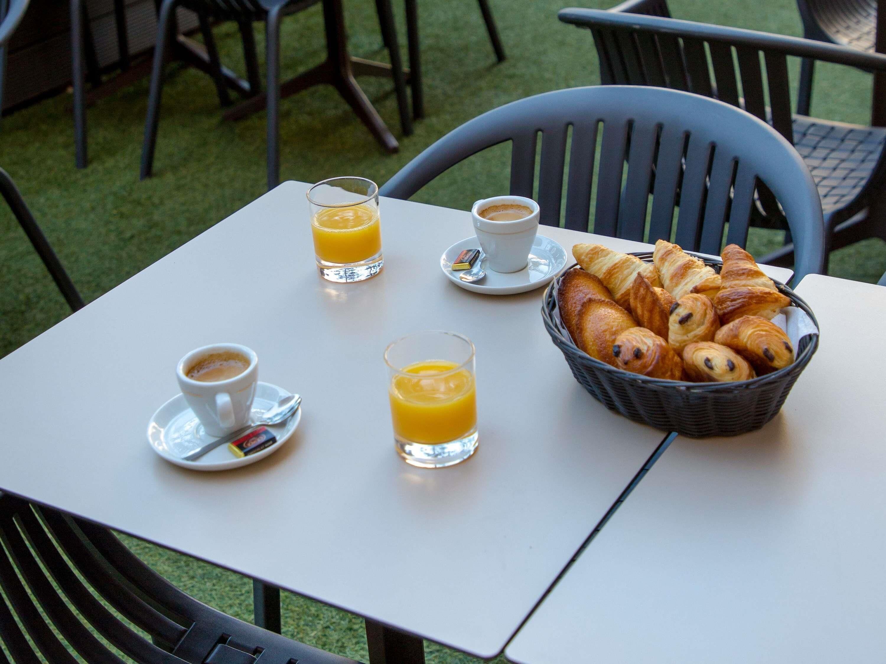 A table with a basket of croissants, two cups of coffee, and two glasses of orange juice.